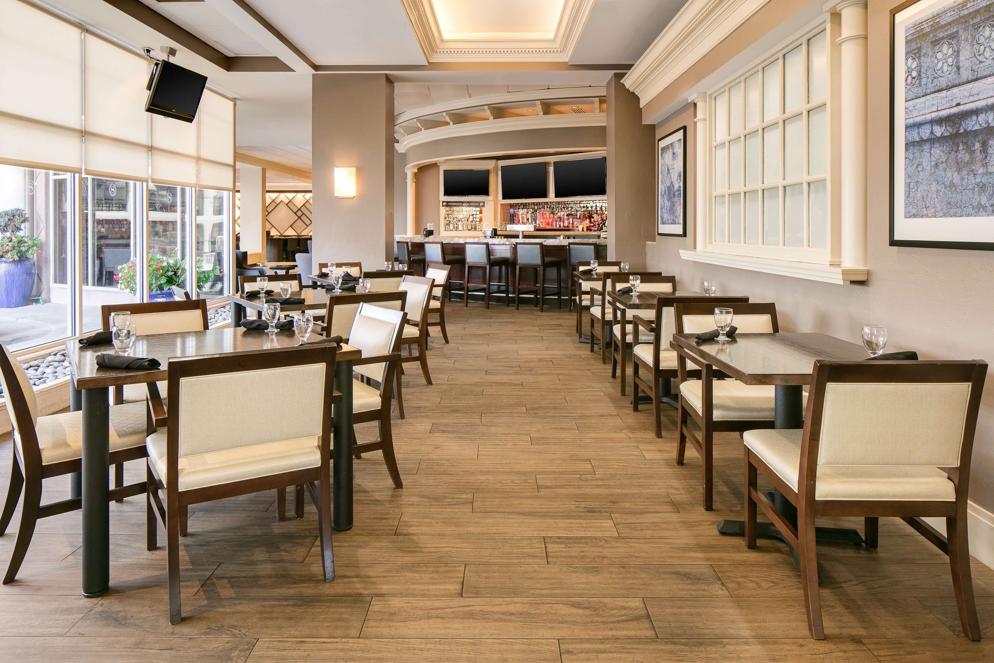 A restaurant with wooden tables and chairs, a bar area, and large windows.