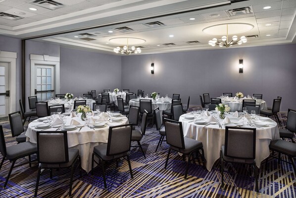 Un salón de conferencias con varias mesas redondas dispuestas para comer, equipado con sillas y mesas, y una alfombra estampada.