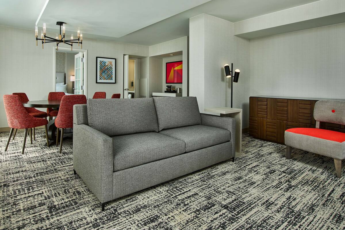 Ein modernes Wohnzimmer mit einem grauen Sofa, roten Sesseln, einem schwarz-weißen Teppich und einer Holzkabine.
