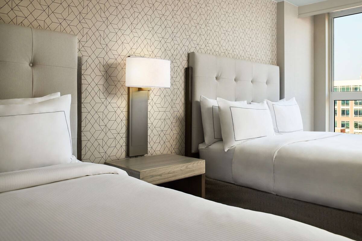 Ein Hotelzimmer mit zwei Betten, einem Nachttisch mit Lampe und einer Wand mit geometrischem Muster.
