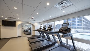 Une salle de sport avec des tapis de course alignés en rangées, de grandes fenêtres et une vue sur un espace extérieur enneigé.