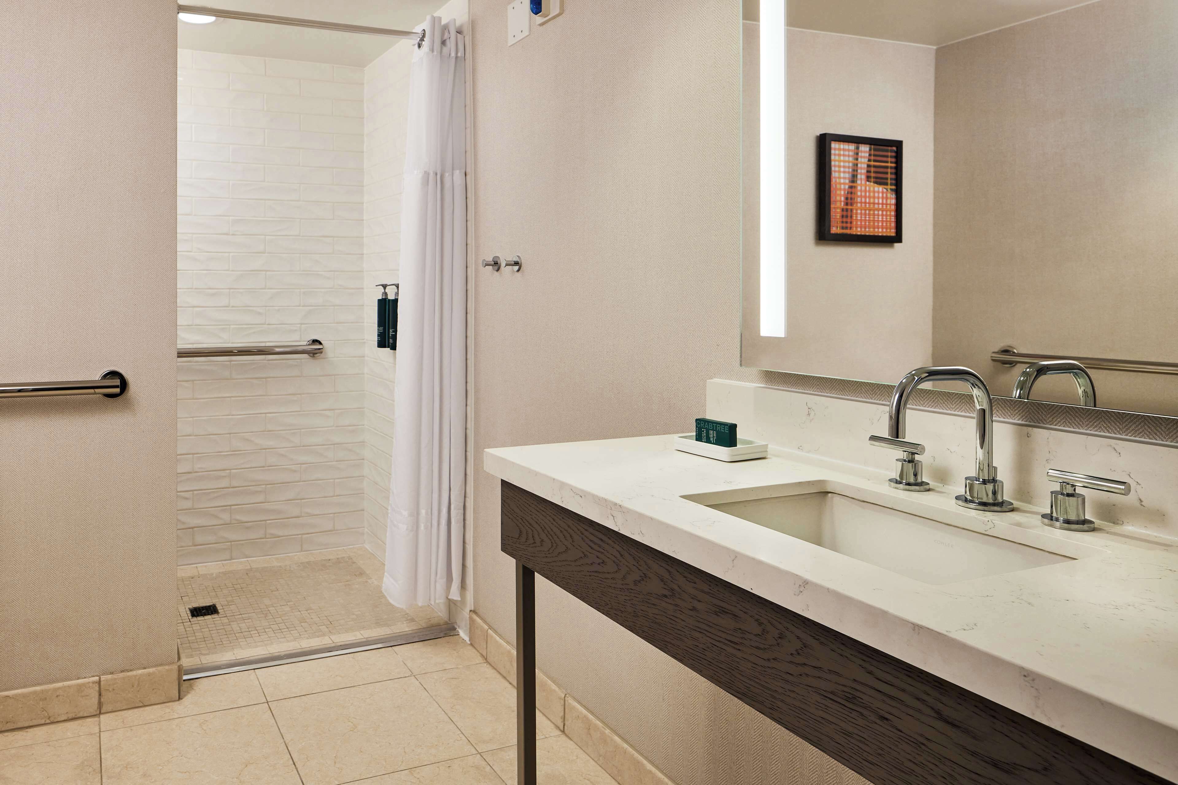 Un baño moderno con ducha, un lavabo de dos grifos y un espejo.