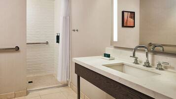 Un baño moderno con ducha, un lavabo de dos grifos y un espejo.