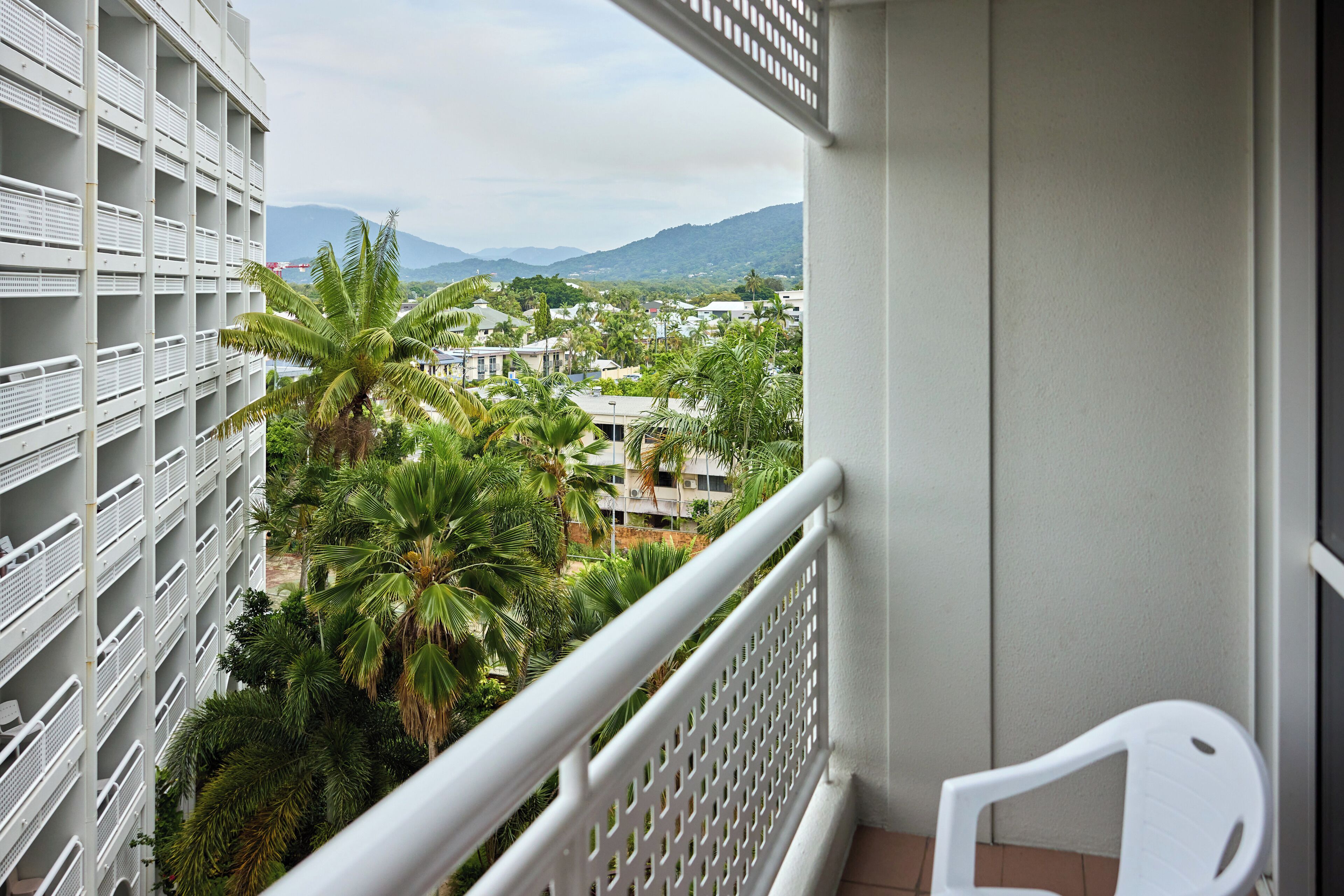 A balcony with a view of a residential area, including houses and palm trees, and a mountain range in the distance.