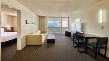 A hotel room with a bed, a sofa, a desk with chairs, a television, and a balcony with a view.