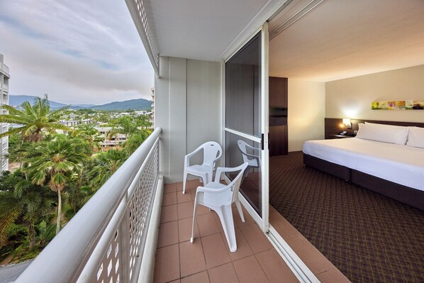 A balcony with a bed, a chair, and a view of palm trees and buildings.