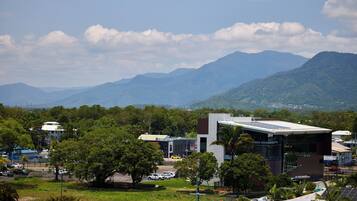 A modern building with a flat roof and large windows, surrounded by lush greenery and mountains in the background.