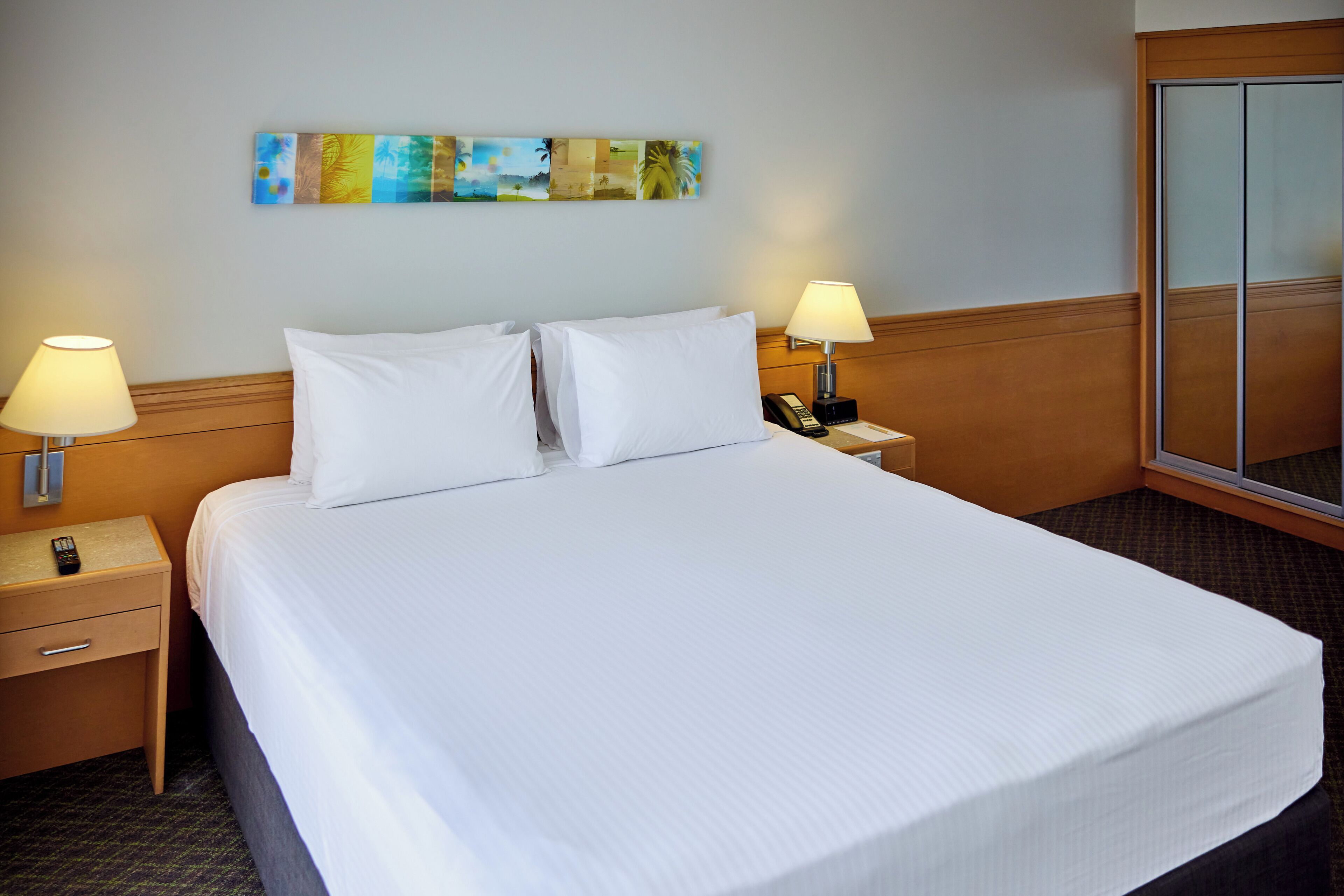A hotel room with a large bed, two bedside tables with lamps, a phone, and a mirror.