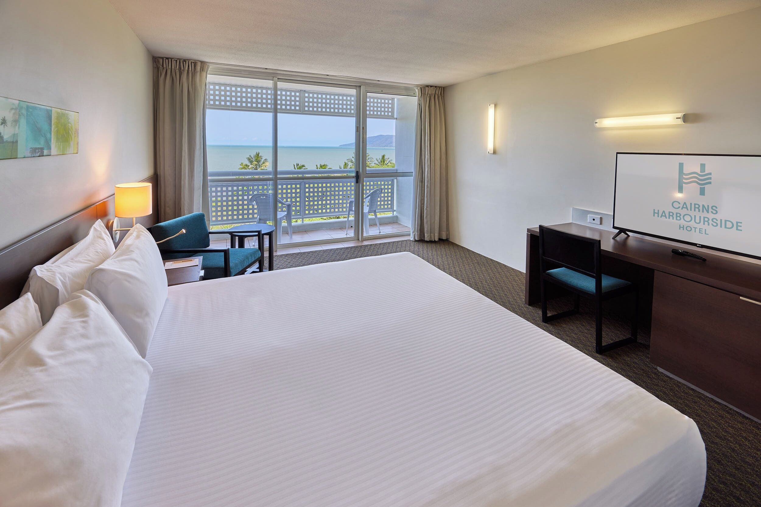 Une chambre d’hôtel avec un grand lit, un bureau, une chaise, une télévision et un balcon avec vue sur la mer.