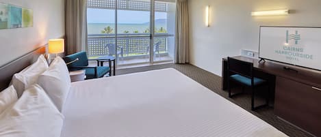 Une chambre d’hôtel avec un grand lit, un bureau, une chaise, une télévision et un balcon avec vue sur la mer.