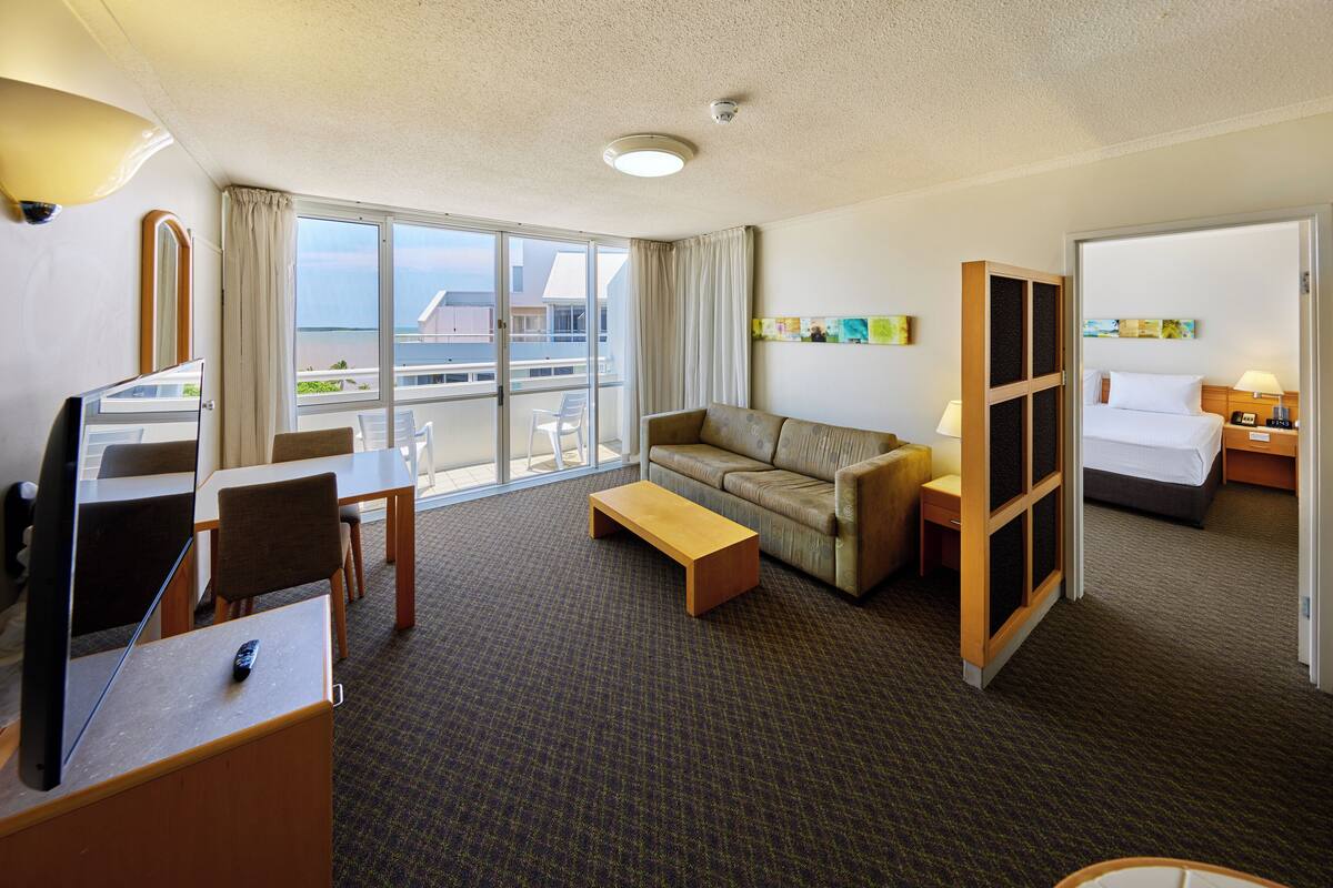 Habitación de hotel con sofá, una mesita, escritorio con computadora, cama y balcón con vista al mar.