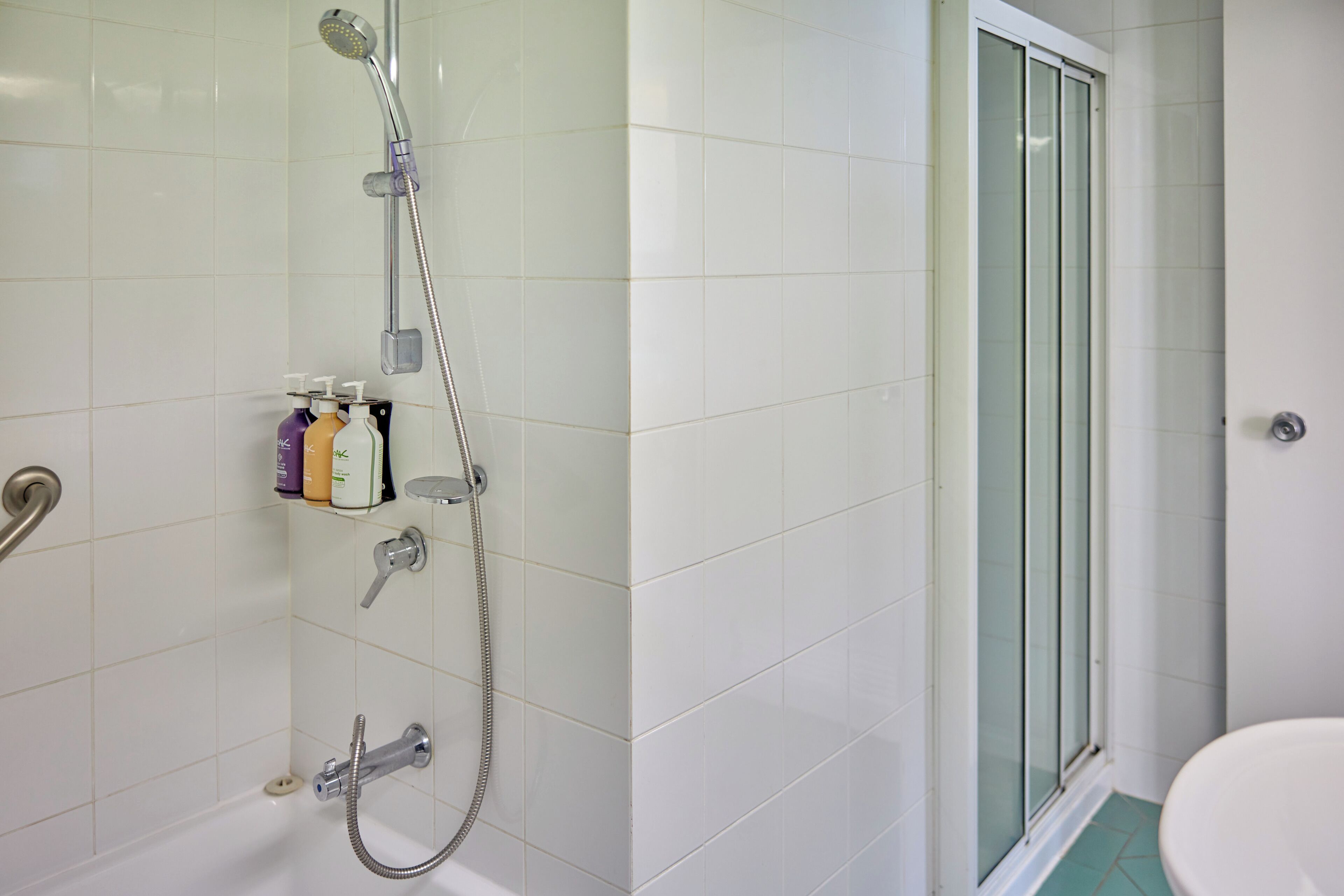 A bathroom with a shower, toilet, and a shelf with toiletries.