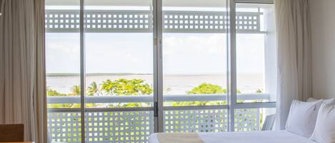 A hotel room with a large bed, a view of the sea, and a balcony with a lattice screen.