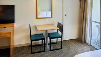 A hotel room with a bed, a desk with a chair, a television, a small table, and a mirror.