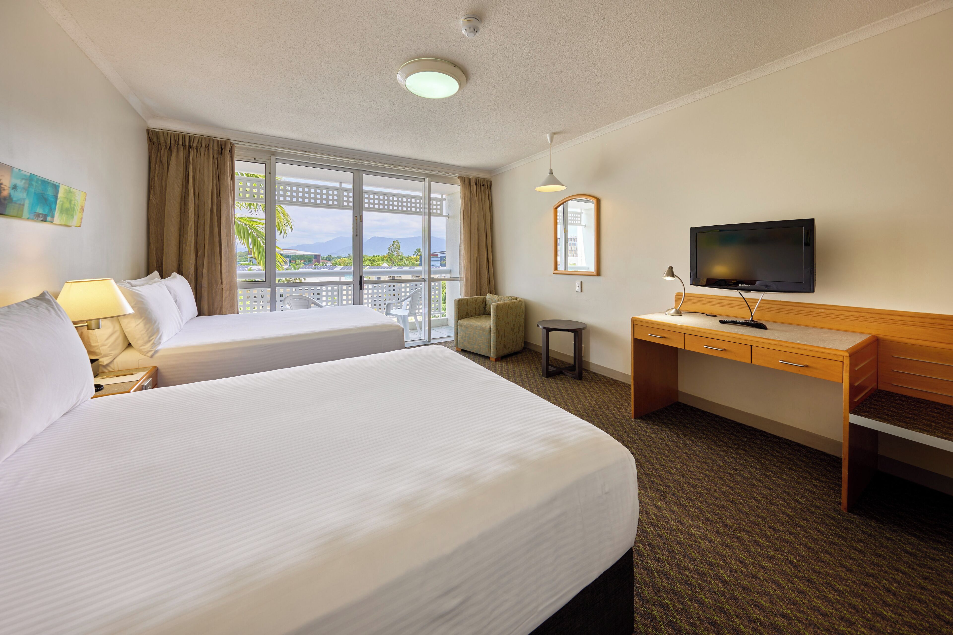 Ett hotellrum med två sängar, ett skrivbord, en tv och en balkong med utsikt över havet.