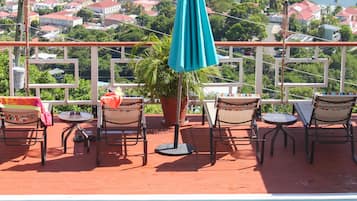 A pool area with a view of the sea and boats, outdoor seating, and a large umbrella.