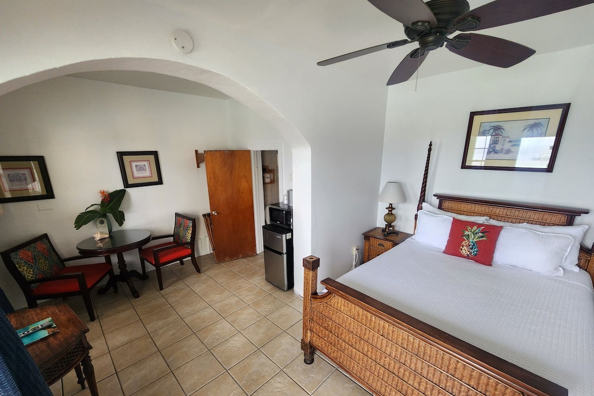 A hotel room with a bed, a desk, a chair, a microwave, and a ceiling fan.