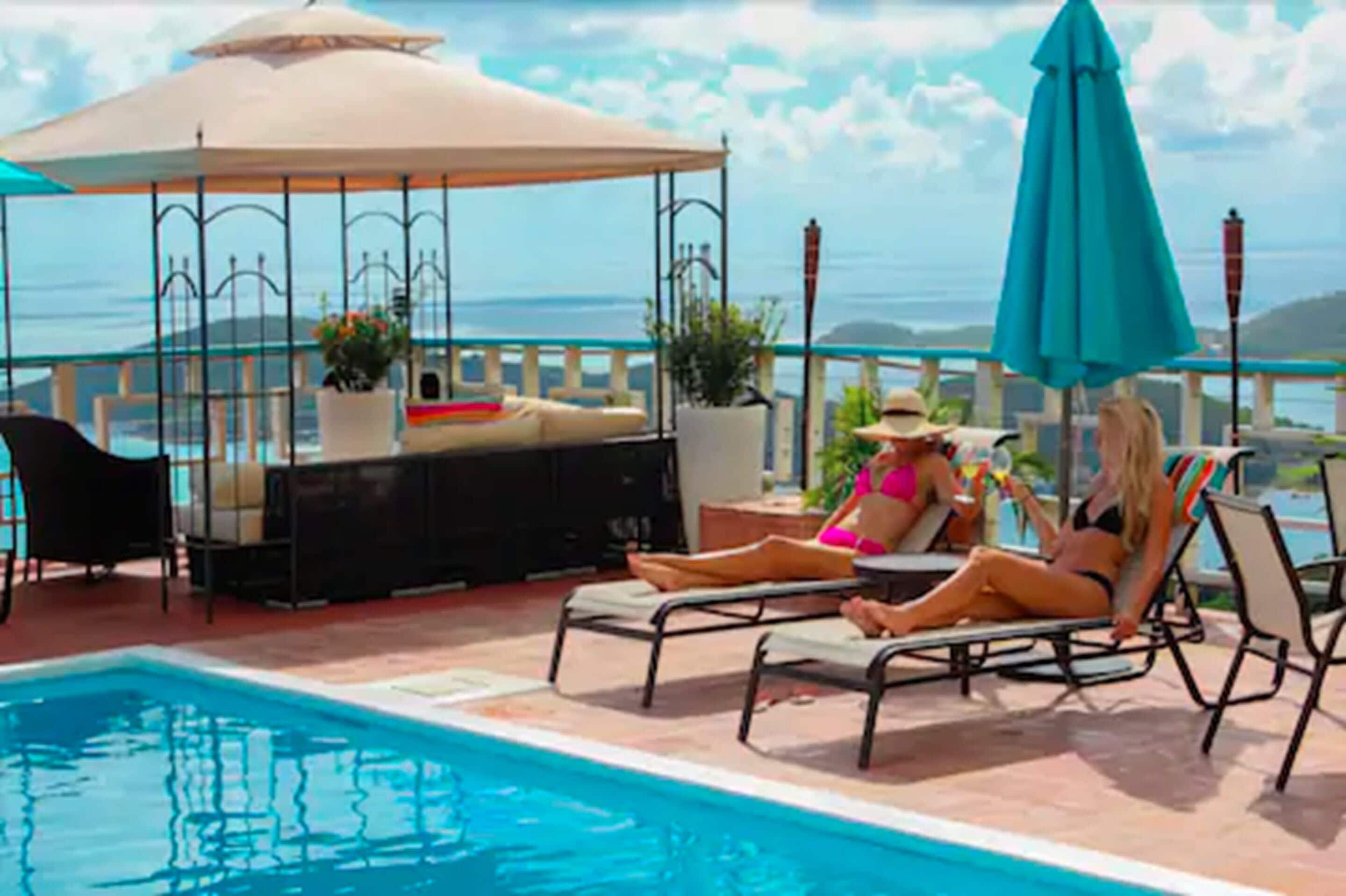 Un área junto a la piscina con sillones, una sombrilla y un espacio de estar con una mesa y sillas.