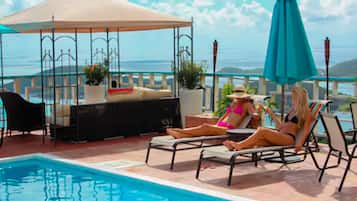 Un área junto a la piscina con sillones, una sombrilla y un espacio de estar con una mesa y sillas.