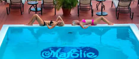 A swimming pool with three people lying on it, surrounded by lounge chairs and a potted plant.