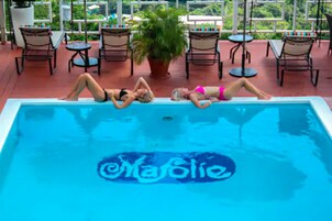 A swimming pool with three people lying on it, surrounded by lounge chairs and a potted plant.