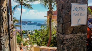 A sign for 'Mafolie Pool Bar' with a view of the ocean and palm trees in the background.