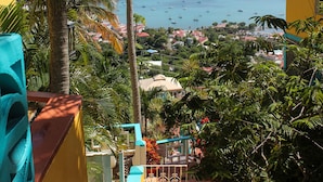 A view from a balcony overlooking a coastal town with a clear sky, palm trees, and a sea view.