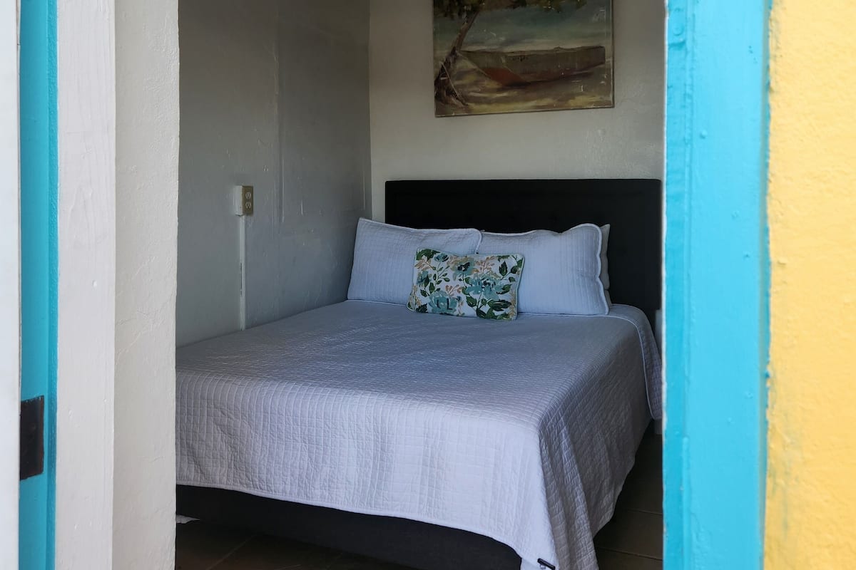 A bedroom with a bed, a ceiling fan, and a painting on the wall.