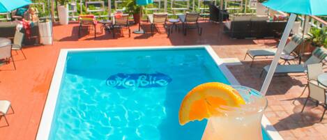 A poolside area with a drink, chairs, and umbrellas.