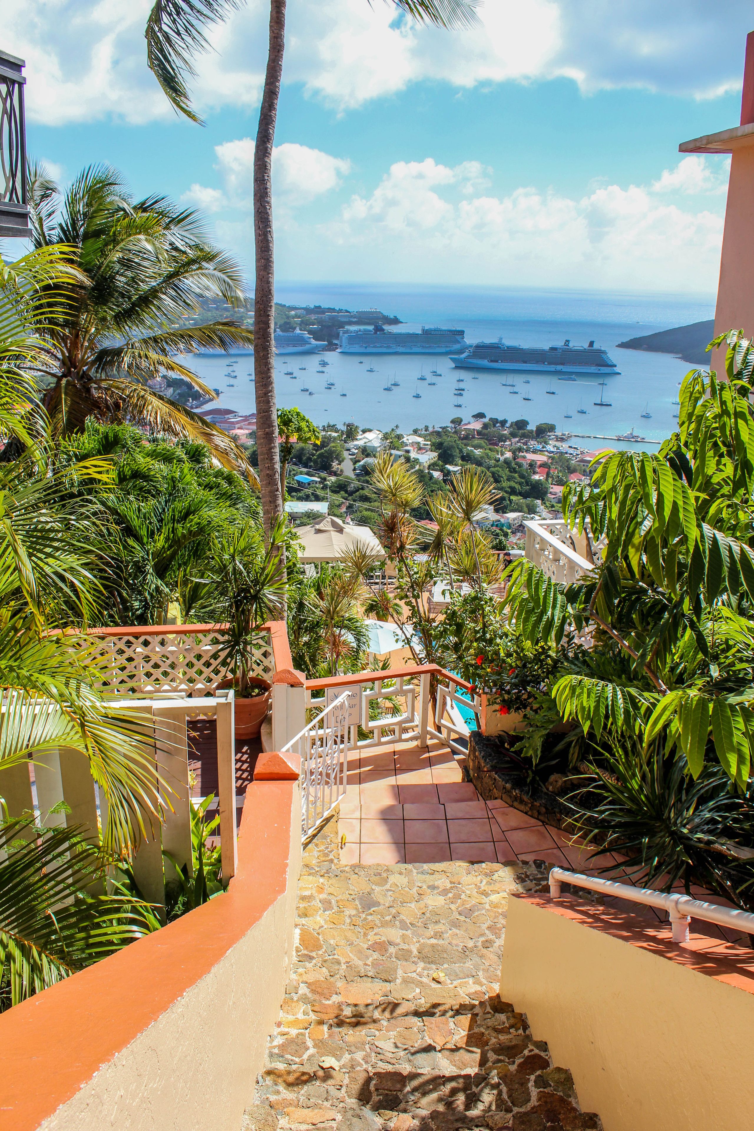 A staircase leading to a balcony overlooking a coastal town with boats and greenery.