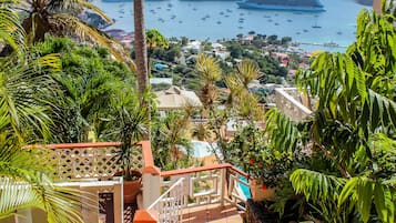 A staircase leading to a balcony overlooking a coastal town with boats and greenery.