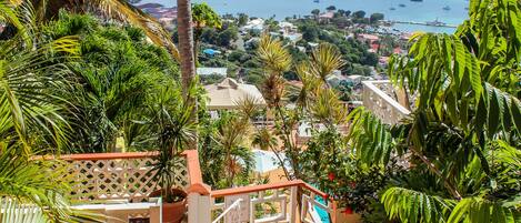 A staircase leading to a balcony overlooking a coastal town with boats and greenery.