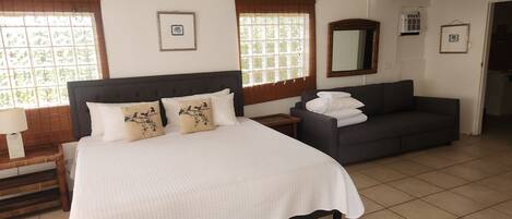 A bedroom with a bed, a sofa, a ceiling fan, and two windows with blinds.