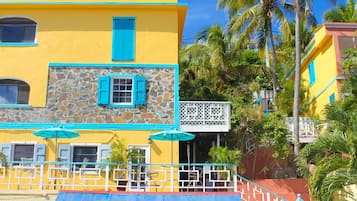 Un área junto a la piscina con un edificio amarillo, un muro de piedra y una palmera.
