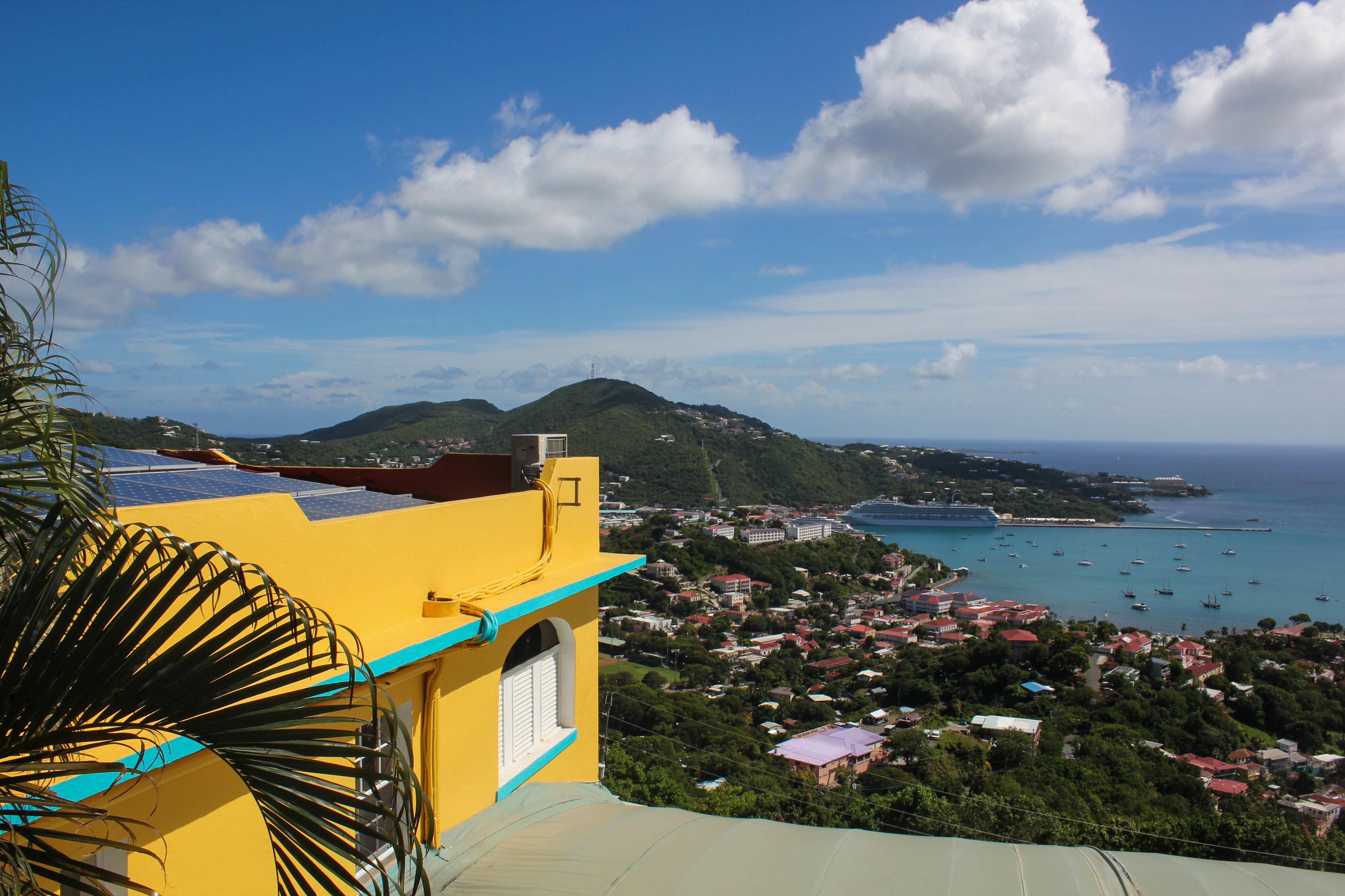A coastal town with a prominent yellow building, lush greenery, and a clear view of the sea with boats.