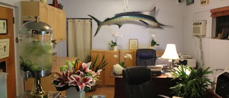 A reception desk with a drink dispenser, a framed welcome sign, and a decorative fish on the wall.