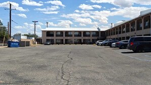 A parking lot with several cars, a building with multiple windows, and a clear sky. - Albuquerque Inn Near Airport I 40 (Albuquerque)
