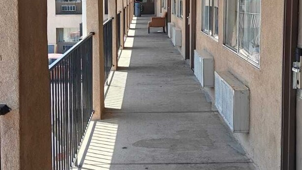 A long corridor with a concrete floor, metal railings, and large windows on both sides. - Albuquerque Inn Near Airport I 40 (Albuquerque)