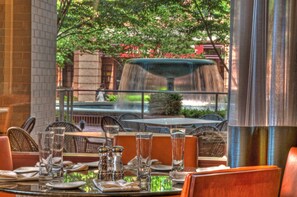 Un espace extérieur aménagé pour les repas, avec des tables pour deux personnes, une cascade en arrière-plan et un mur de briques sur un côté.
