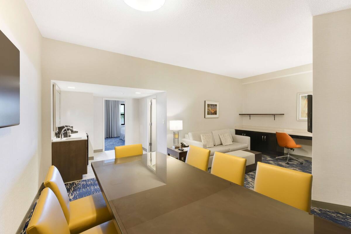 A hotel room with a dining area, a sofa set, a desk, and a TV.