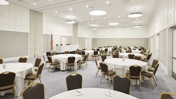 Un salón de conferencias con mesas y sillas redondas, paredes blancas y suelo alfombrado.