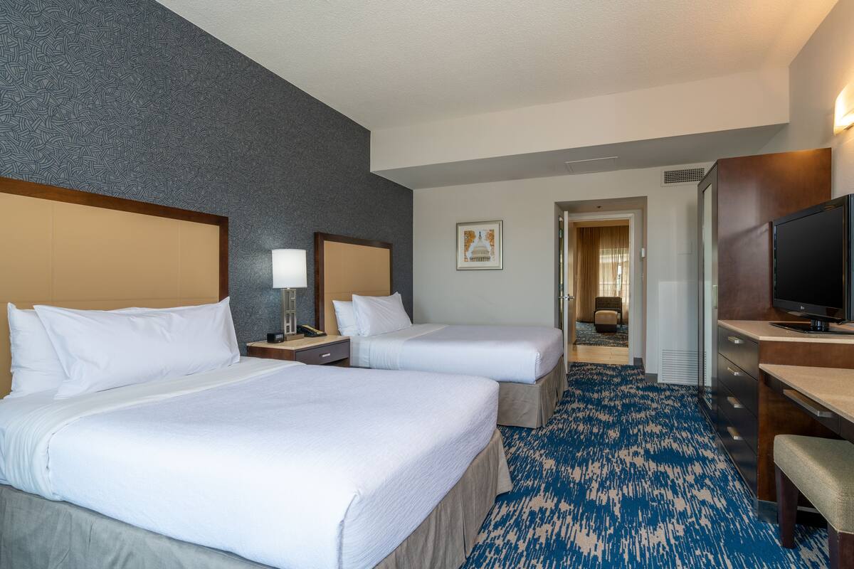 A hotel room with two beds, a desk with a TV, and a bathroom visible through an open door.