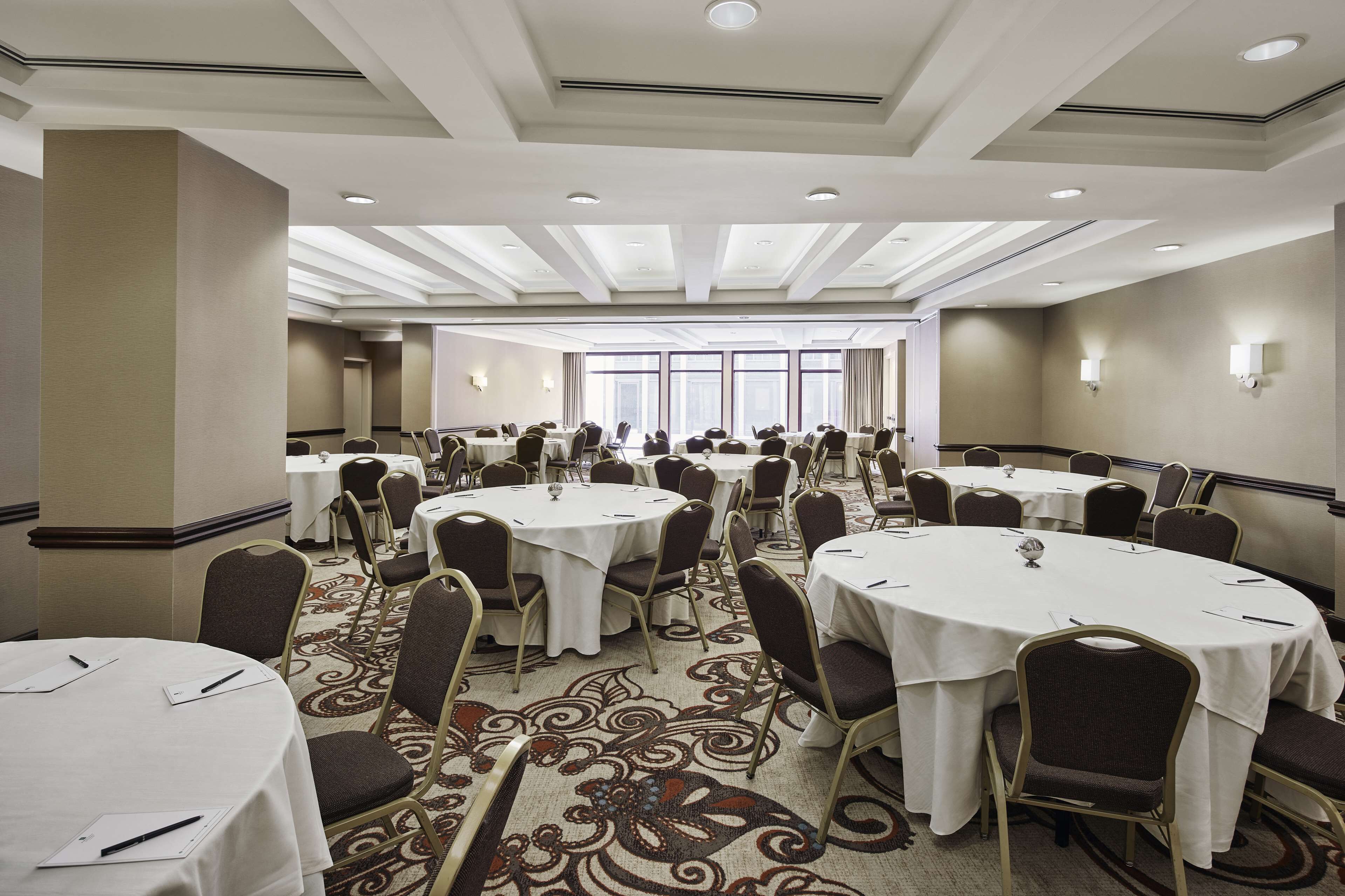 A conference room with multiple round tables, chairs, and a carpeted floor.