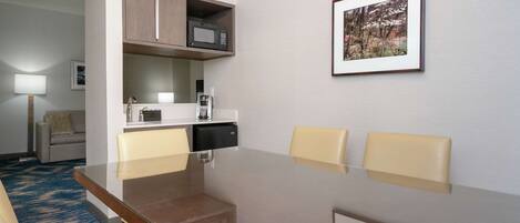 A hotel room with a dining table, two chairs, a microwave, a coffee maker, and a framed picture on the wall.