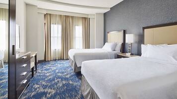 A hotel room with two beds, a desk, and a large window with curtains.