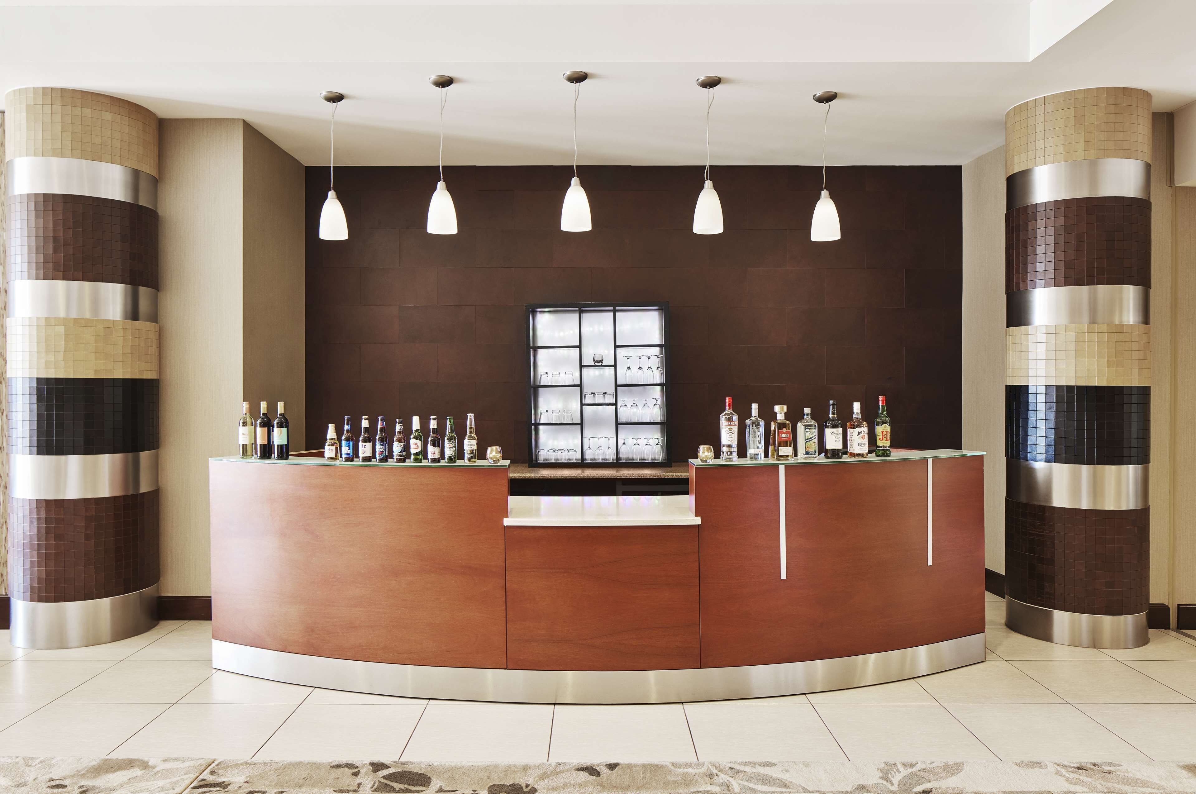 A reception area with a curved wooden counter, hanging pendant lights, and a display of bottled beverages.