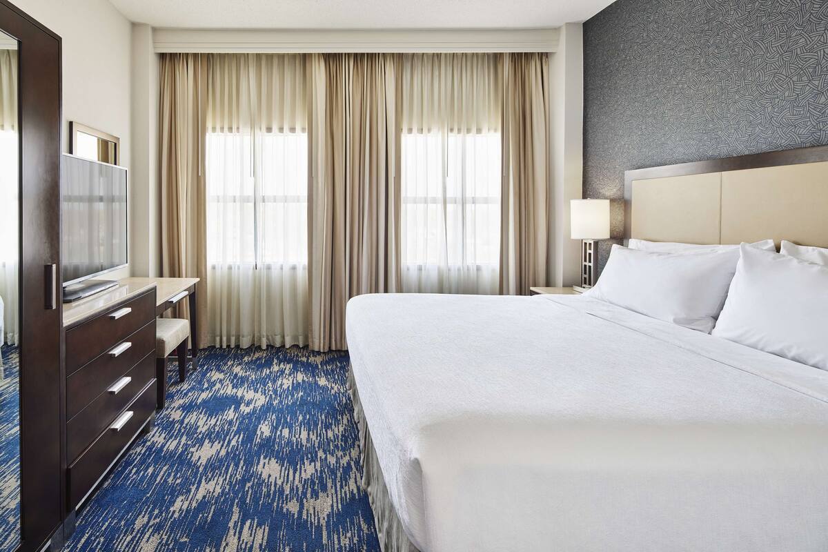 A hotel room with a large bed, a desk, a TV, and a window with curtains.