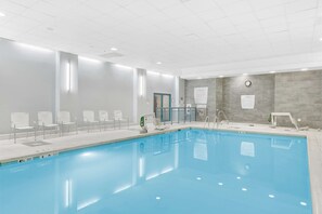 Una piscina con solárium de baldosas, sillas y vestuario.