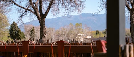 Un área de estar al aire libre con mesas y sillas, una valla de madera y vistas a montañas al fondo.