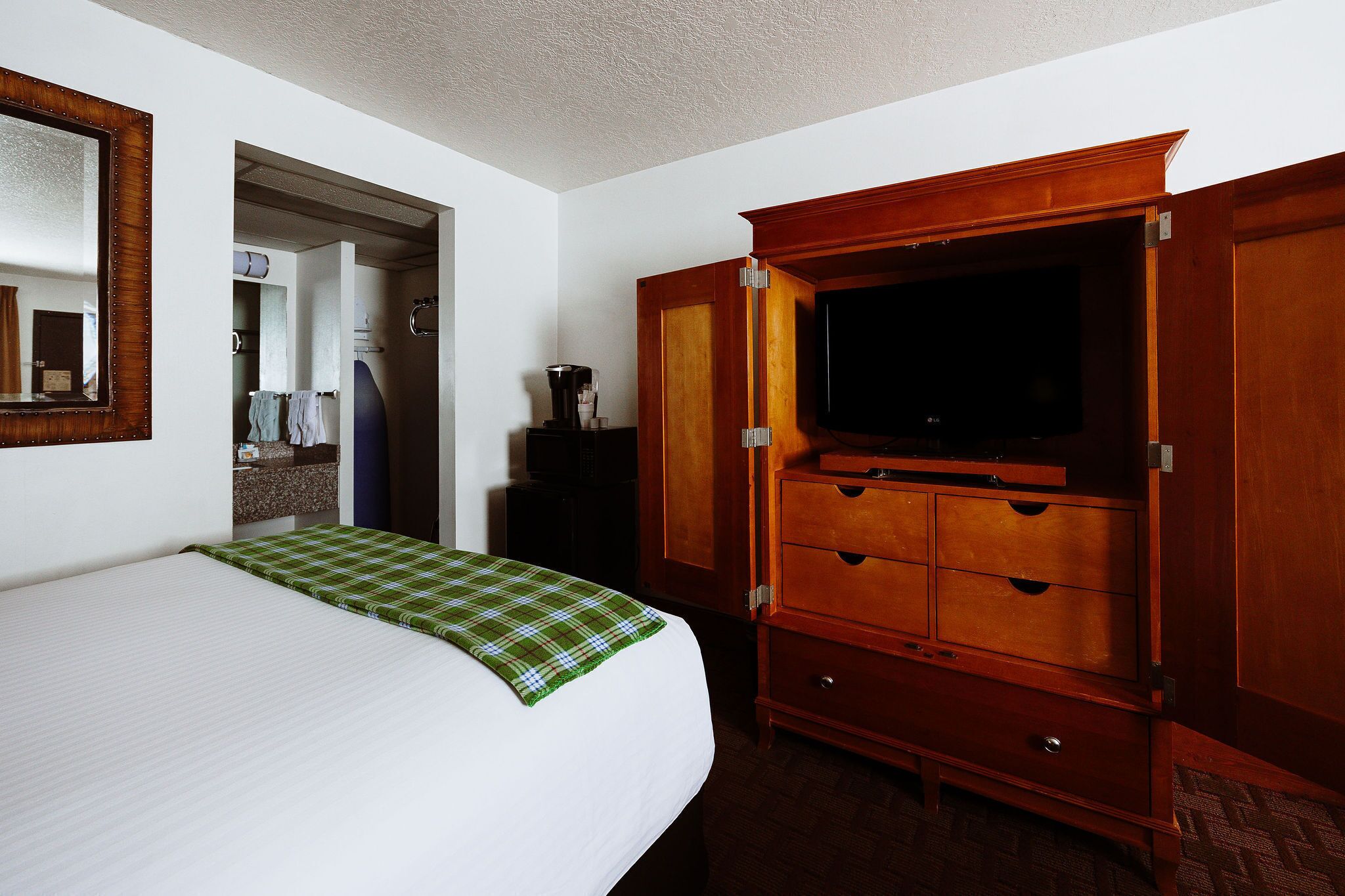 A hotel room with a bed, a wooden dresser, a television, and a bathroom visible through an open door.